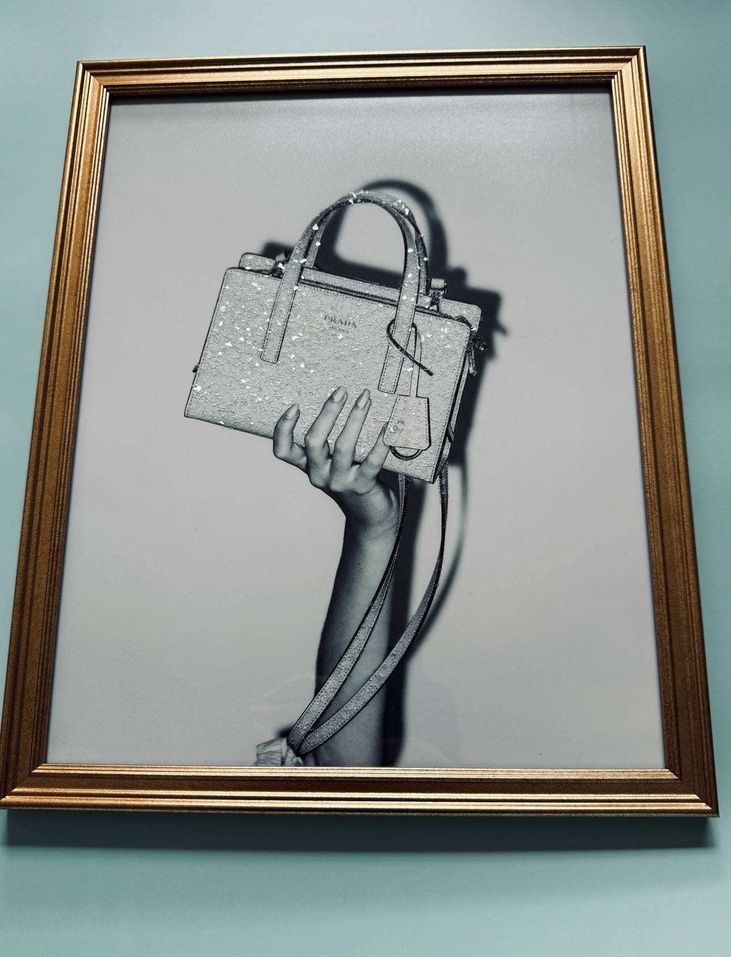 A photograph of a manicured hand holding a sparkle bedazzled Prada handbag.