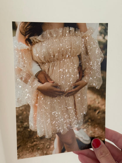 A photograph with a pregnant woman with sparkle embellished dress and and partner holding mom's belly.